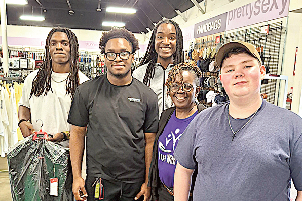 Ms. Hill smiles with male students who received prom suits.